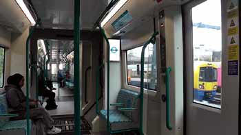 Inside DLR B23 train whilst passing London Overground Class 378 trainStratford International station building night