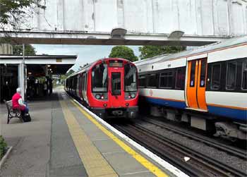District line and Overground North London / Mildmay line trains pass at Kew Gardens station.
